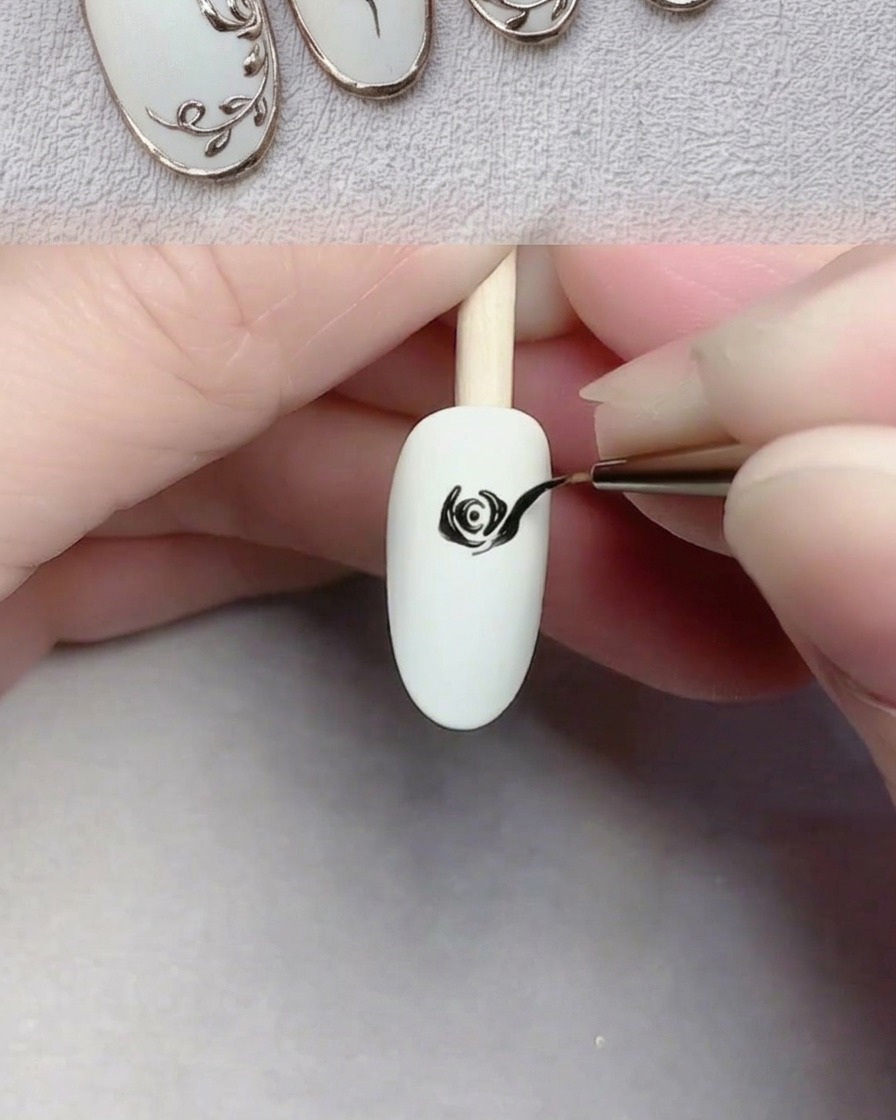 Un pinceau de nail art peignant de grands pétales noirs sur un ongle blanc pour compléter la rose.