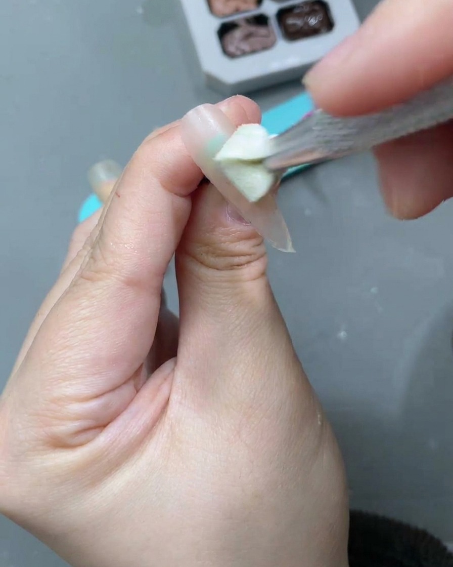 Un pinceau à ongle appliquant un gel cat-eye lune blanche sur la base nude précédemment appliquée.