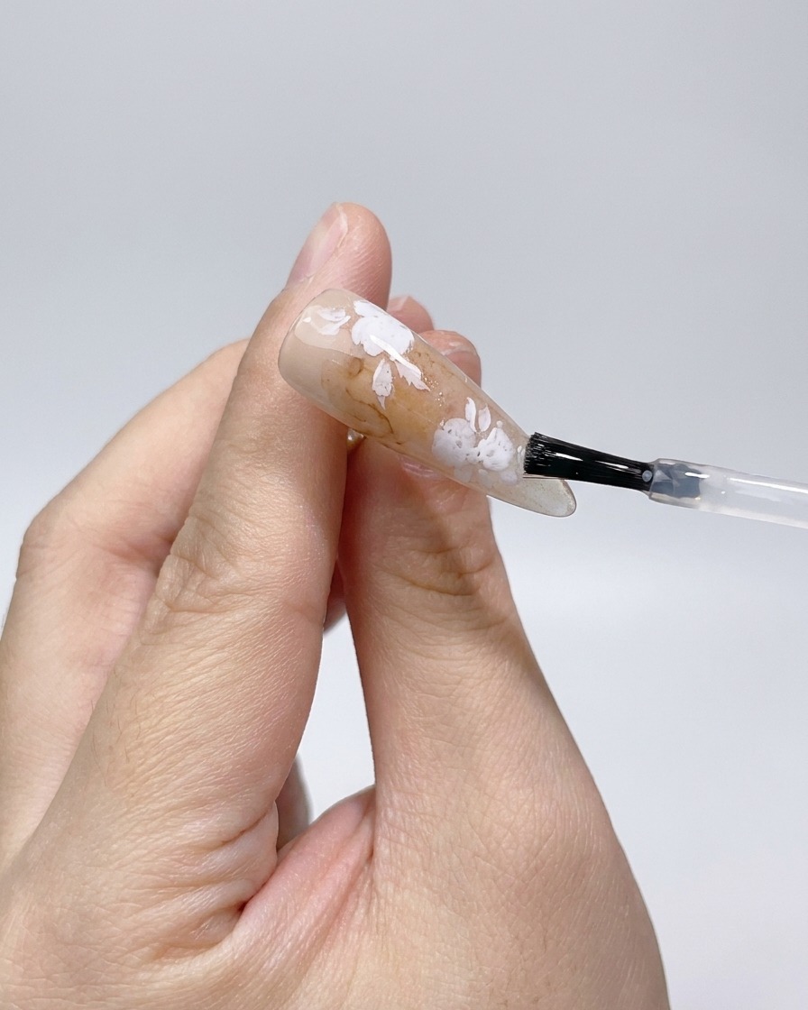 Application dun top coat mat sur les contours de rose blanche sur longle.