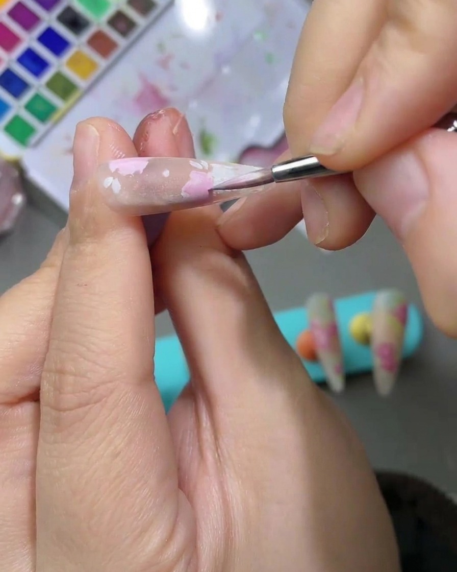 Vue détaillée dun design nail art présentant des feuilles aquarelle vert clair peintes à côté des pétales de rose rose.