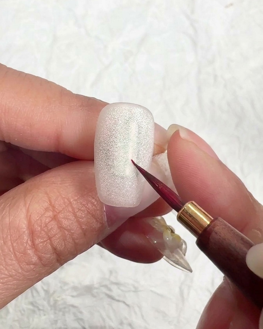 Un pinceau appliquant un top coat mat sur un ongle cat eye.