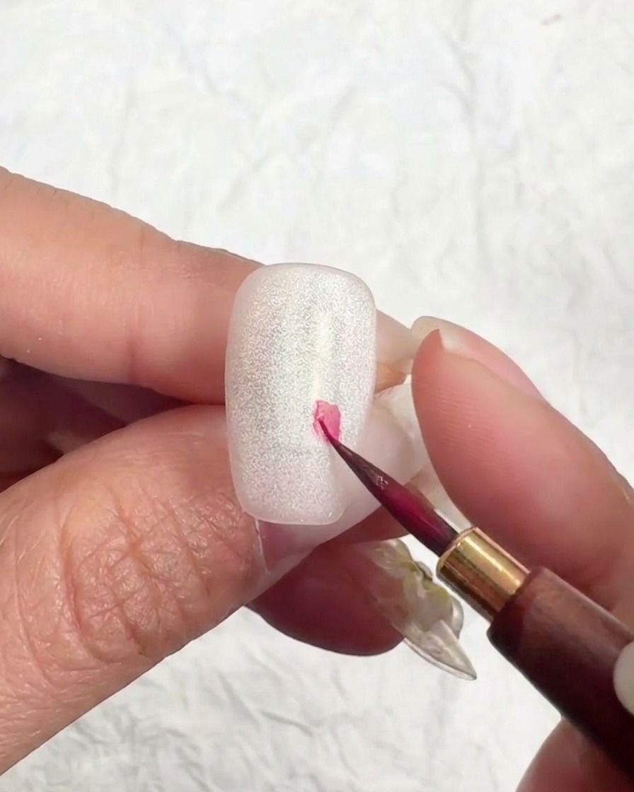 Un pinceau liner déposant un petit point rose pour commencer une fleur.