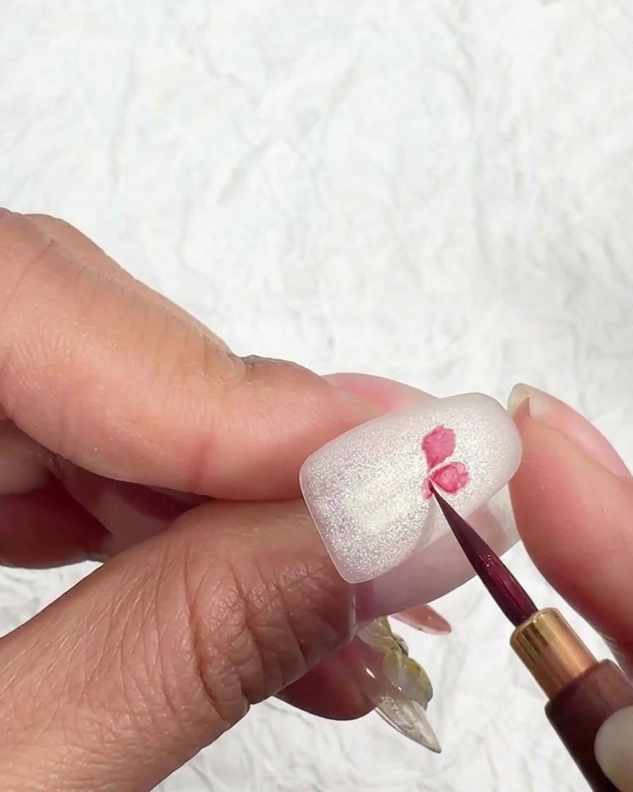 Un pinceau nail art dessinant le cœur dune fleur sur une base mate.