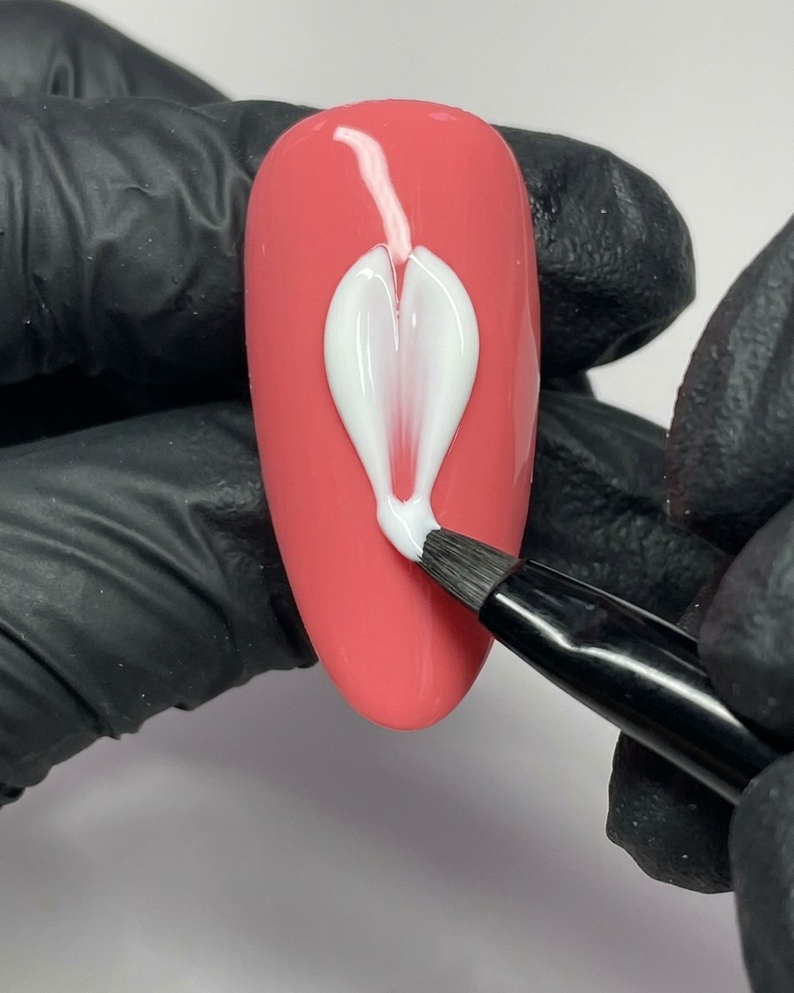 Un pinceau de nail art appliquant du gel blanc pour former le côté gauche dun pétale sur un ongle rose.