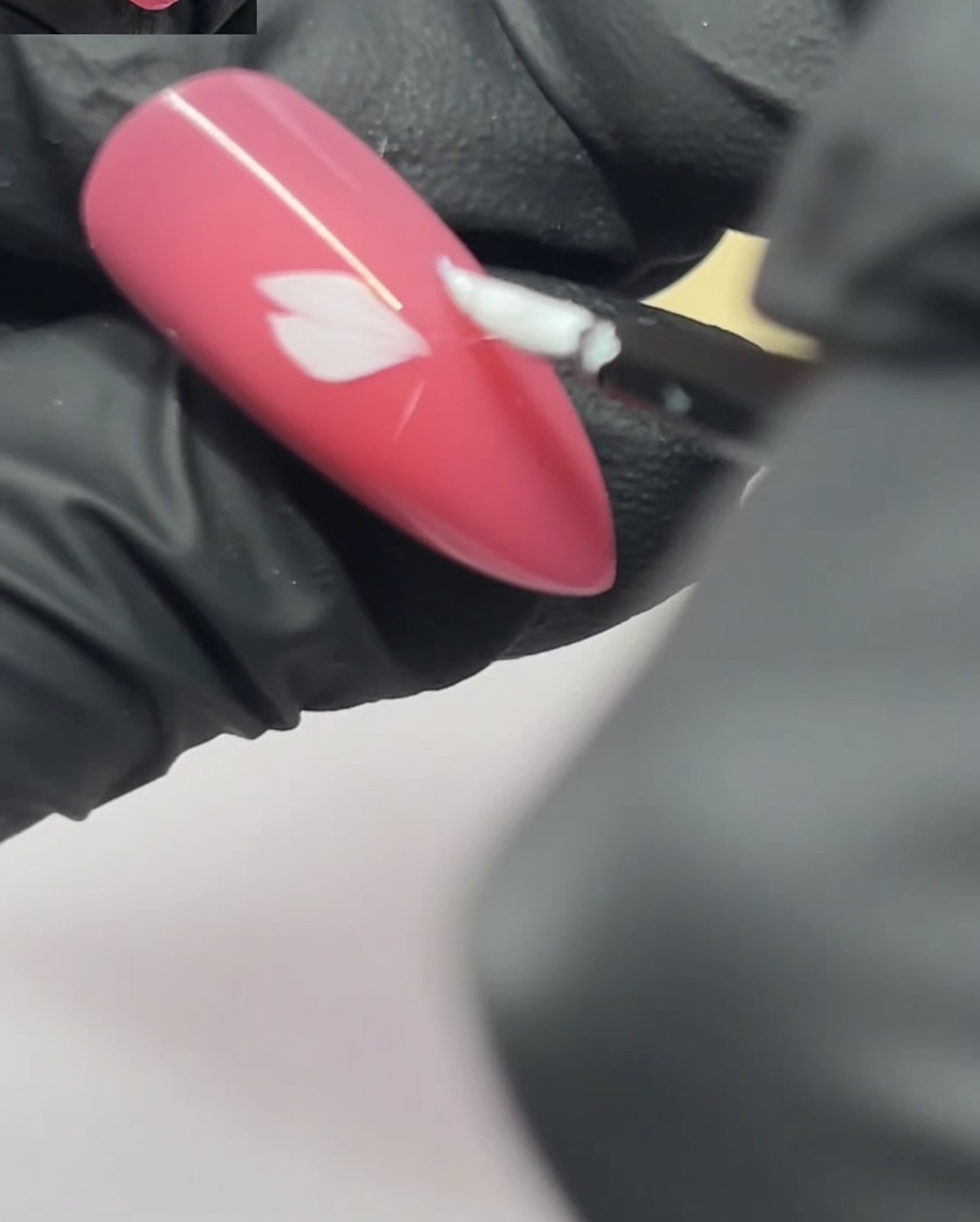 Un pinceau de nail art appliquant un deuxième pétale à côté du premier sur un ongle rose.