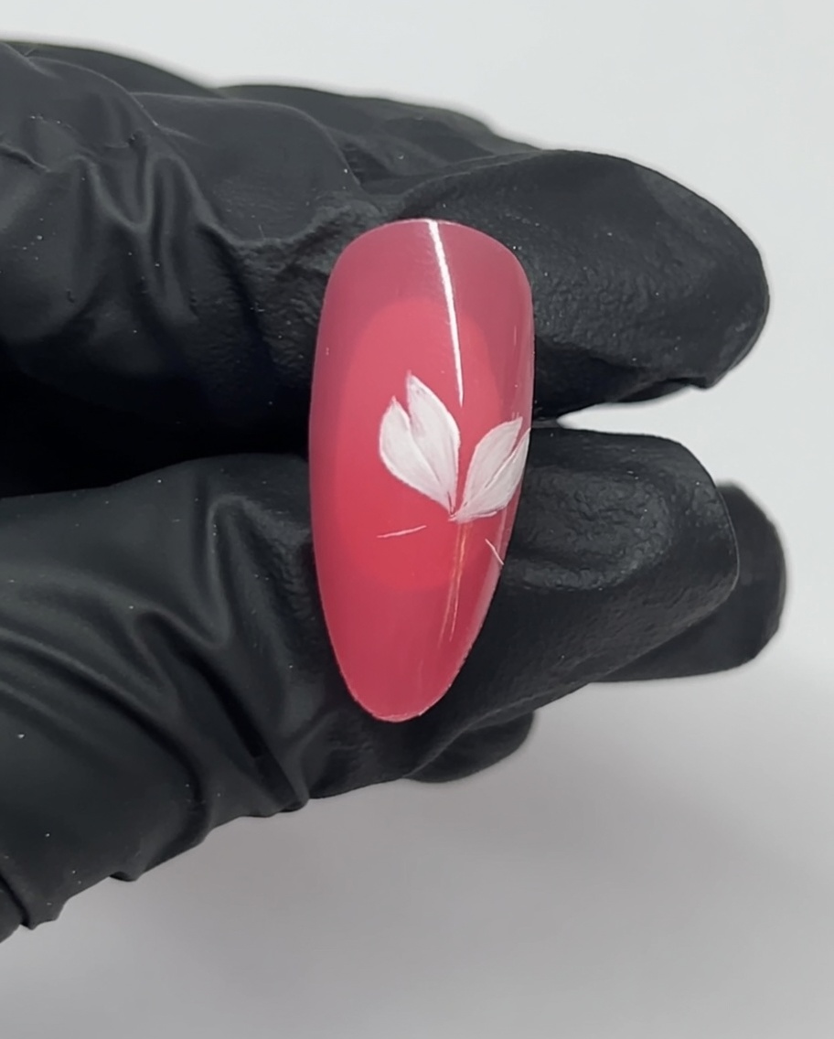 Gros plan sur un ongle montrant trois pétales blancs dun motif fleur de cerisier sur une base rose.