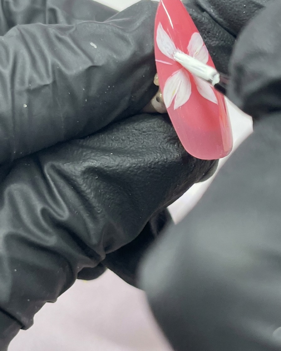 Gros plan sur un ongle avec une fleur de cerisier blanche à cinq pétales peinte sur un fond rose.