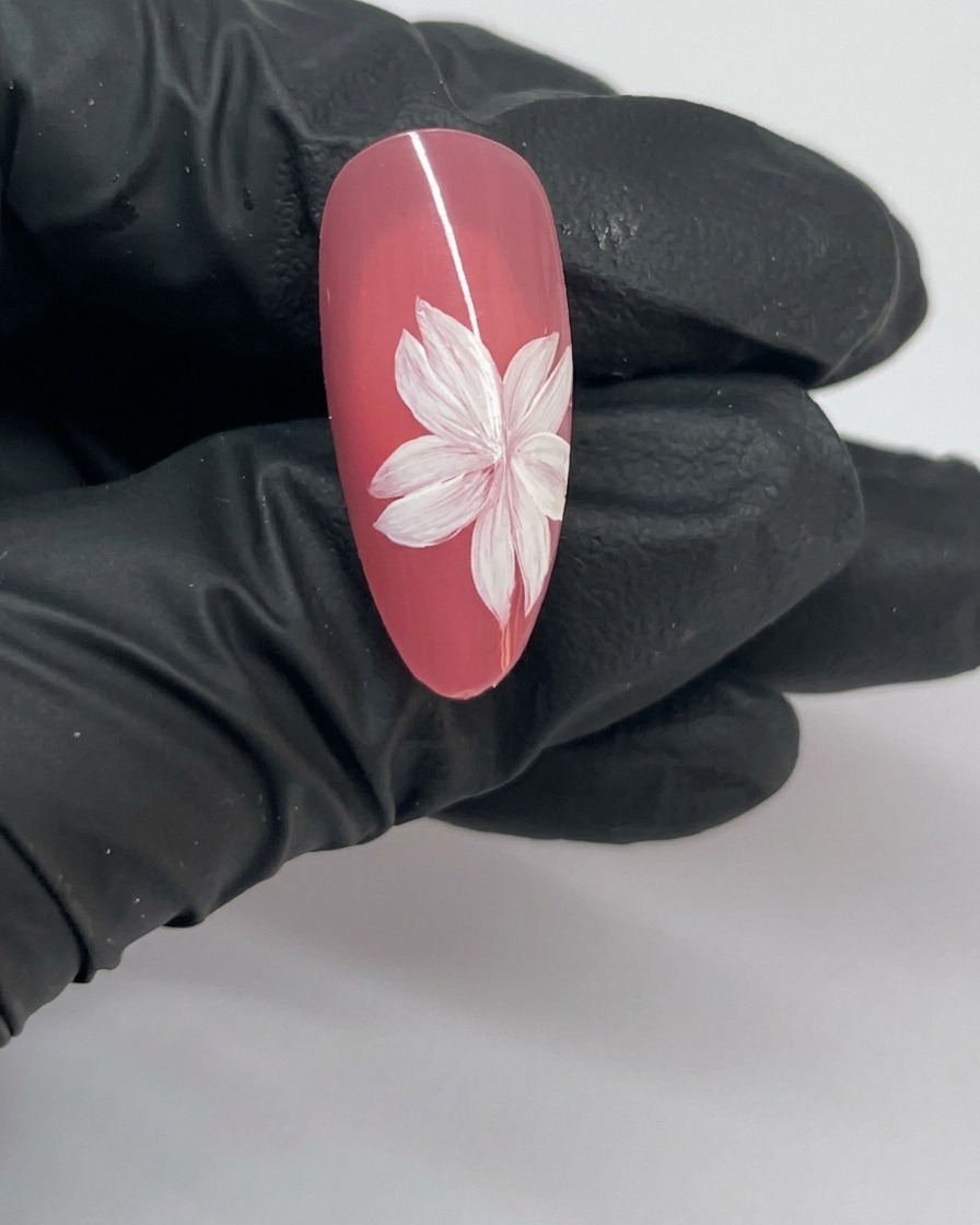 Gros plan dun nail art fleur de cerisier fini avec un centre à étamine blanche.