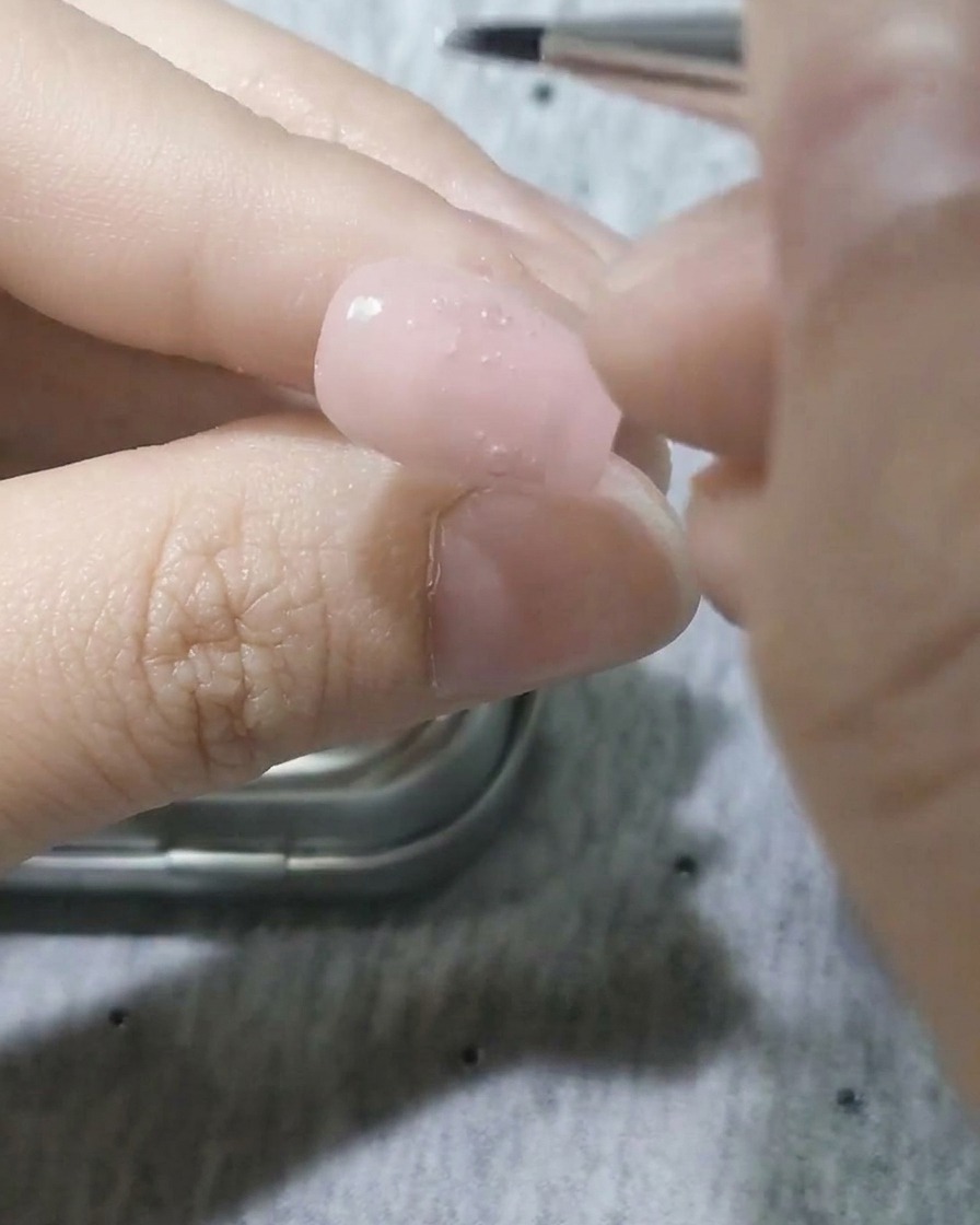 Un pinceau de détail fin appliquant du gel blanc pour former une forme de pétale sur longle.