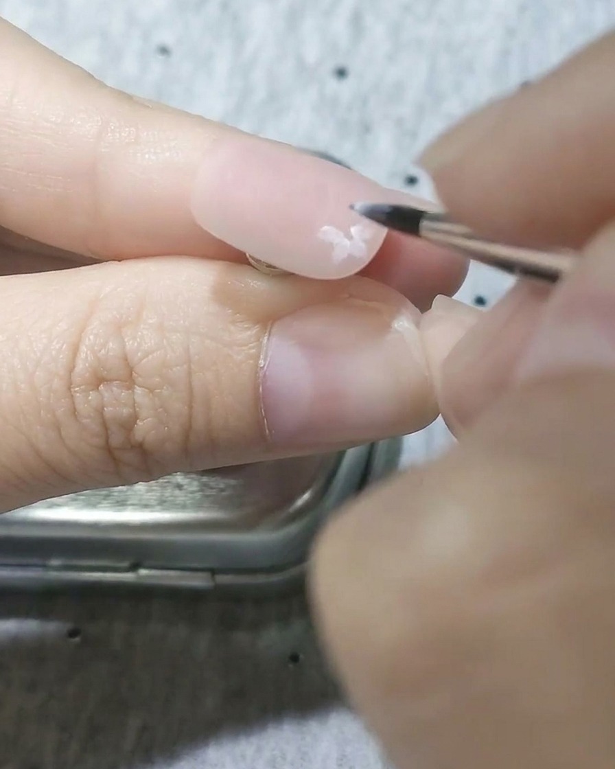 Gros plan dun pinceau fin peignant des pétales de fleurs de cerisier blanches semi-transparentes sur une base dongle rose mate.