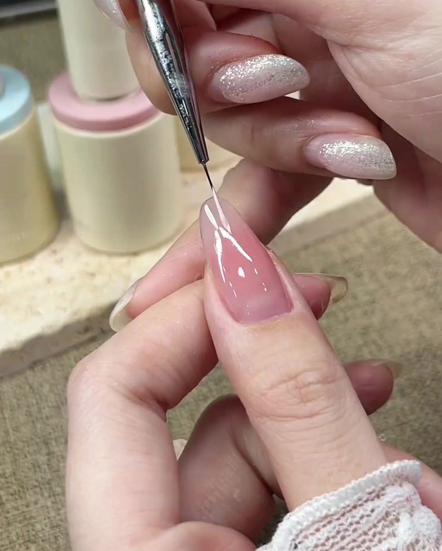 Un pinceau de précision dessine la courbe gauche du sourire de la French manucure avec du gel rose pastel.