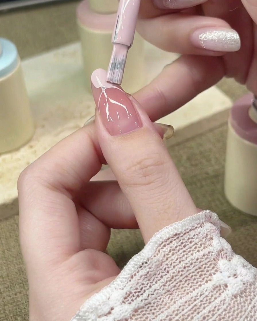 Un pinceau à ongles remplit la zone de la French avec du vernis gel rose pastel.