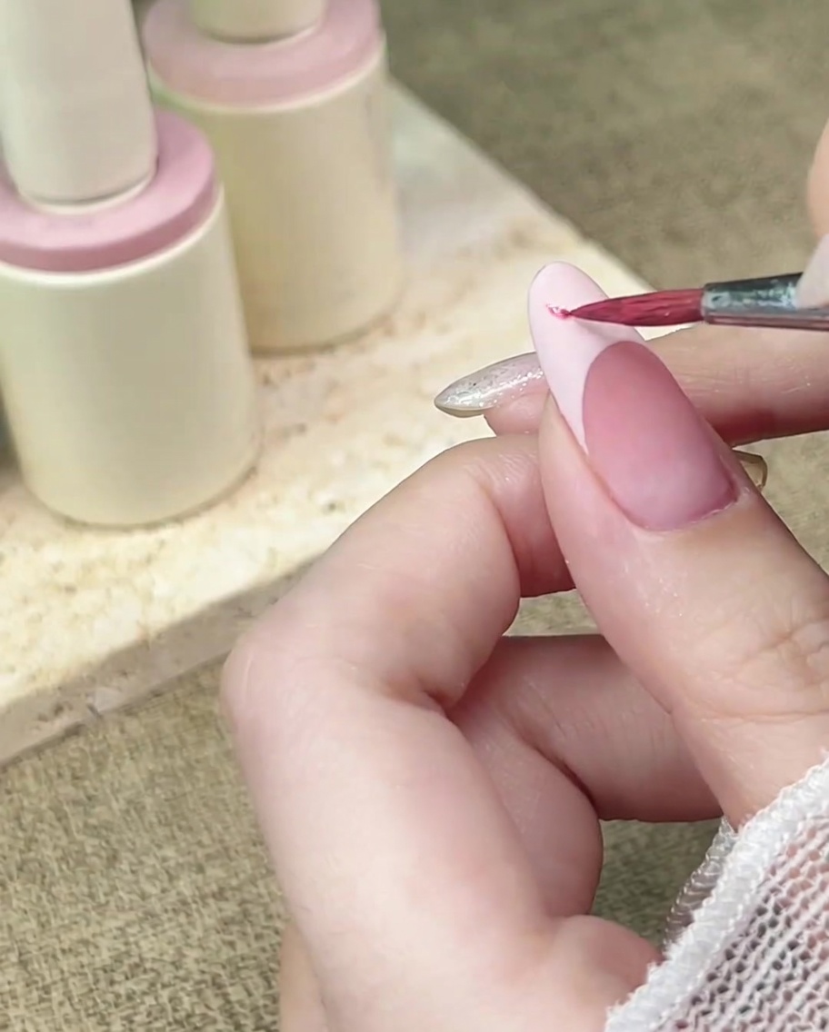 Un pinceau de détail applique de laquarelle rose sur une French manucure au fini mat.