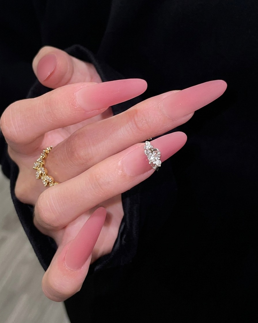 Une main avec de longs ongles rose dégradés posée élégamment sur un fond de manche noire, soulignant la transition du nude diaphane au rose foncé.