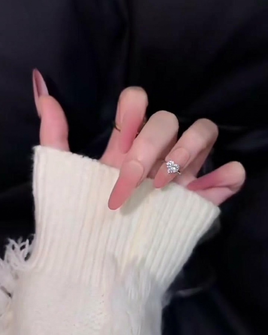 Gros plan sur de longs ongles rose ombrés magnifiquement effilés sur un fond noir, montrant un fini velours doux et diffus.