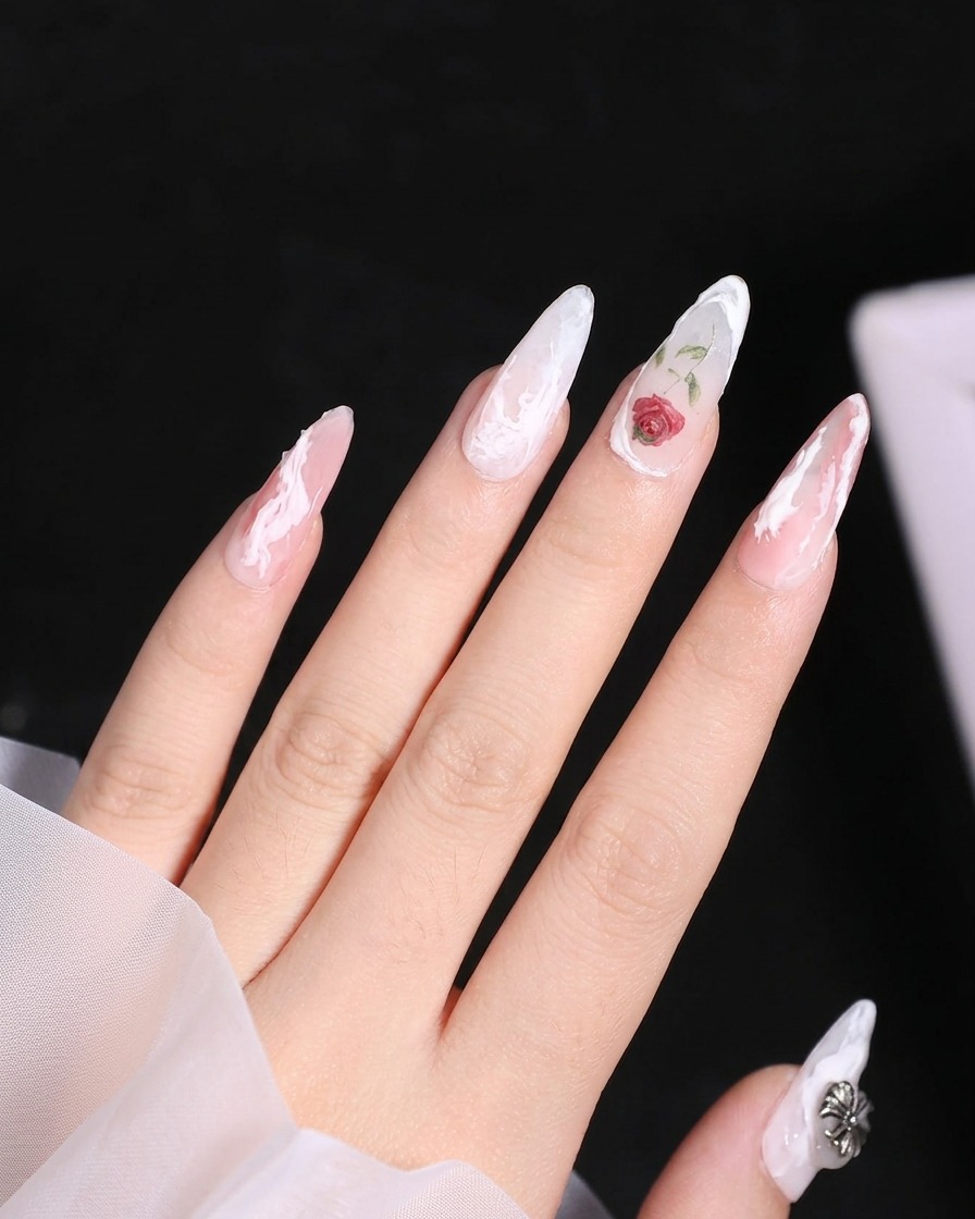 Un gros plan dun ongle avec une rose peinte, et un petit pinceau ajoutant une base de feuille verte à côté de la fleur.