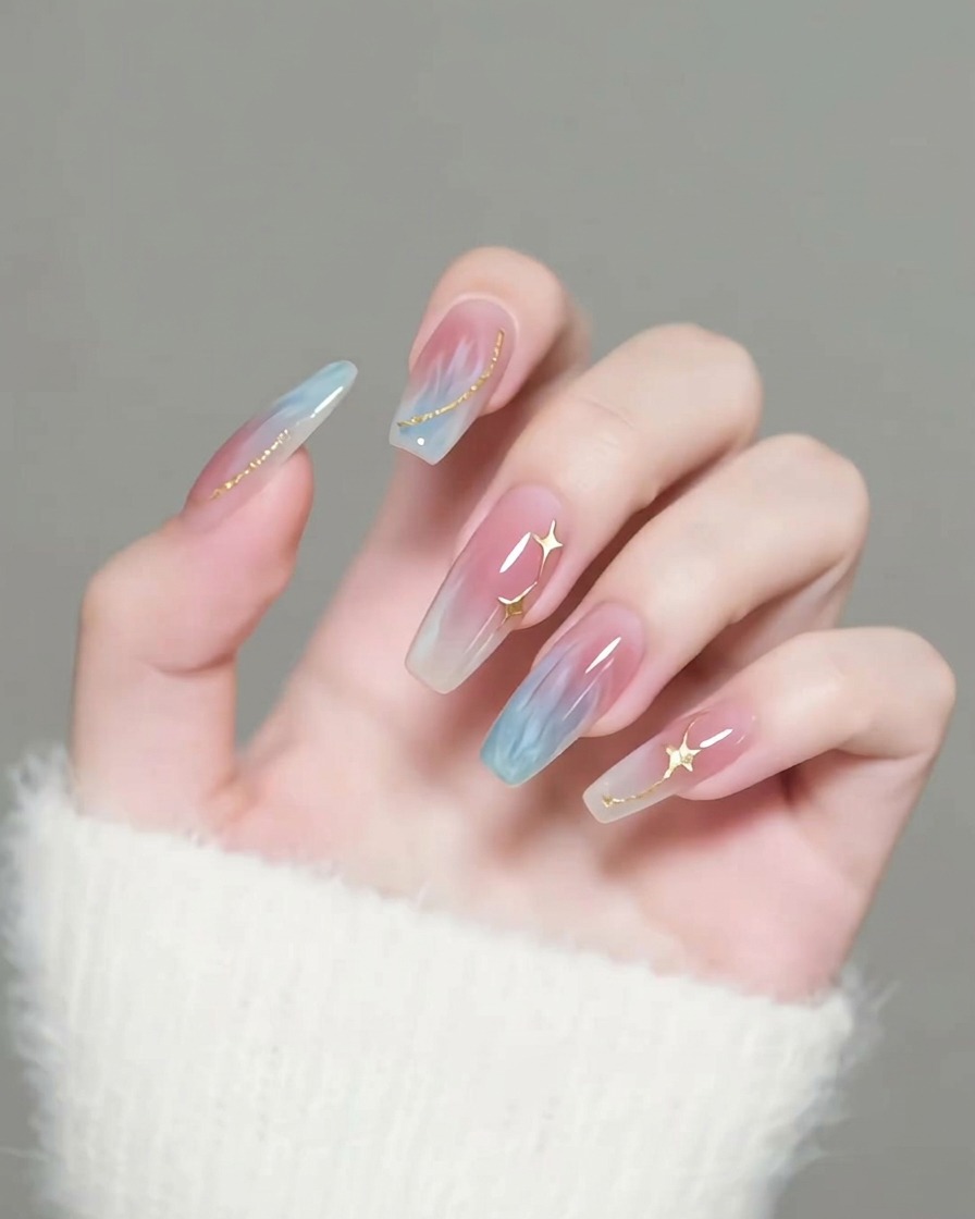 Un pinceau appliquant une couche de finition brillante et transparente sur des ongles décorés détoiles dorées.