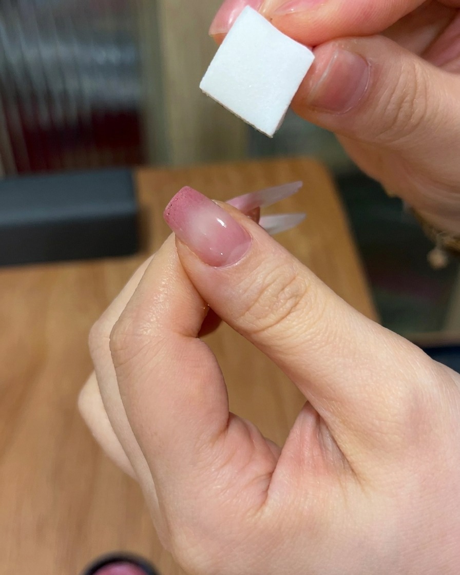 Gros plan montrant une éponge déposant du gel rose sur un ongle, créant un dégradé doux et fondu du bout vers le centre.