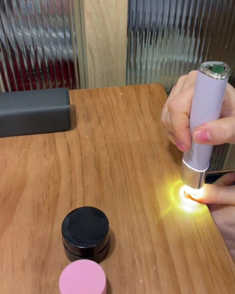 Un ongle placé sous une petite lampe LED portable violette sur une table en bois, pour catalyser le vernis gel.
