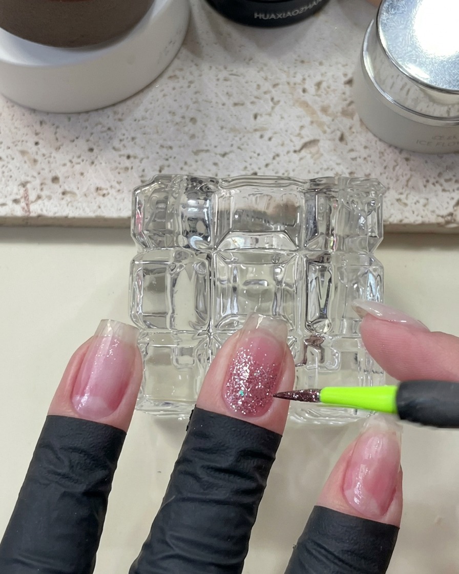 Un pinceau de précision appliquant des paillettes scintillantes roses sur un ongle.