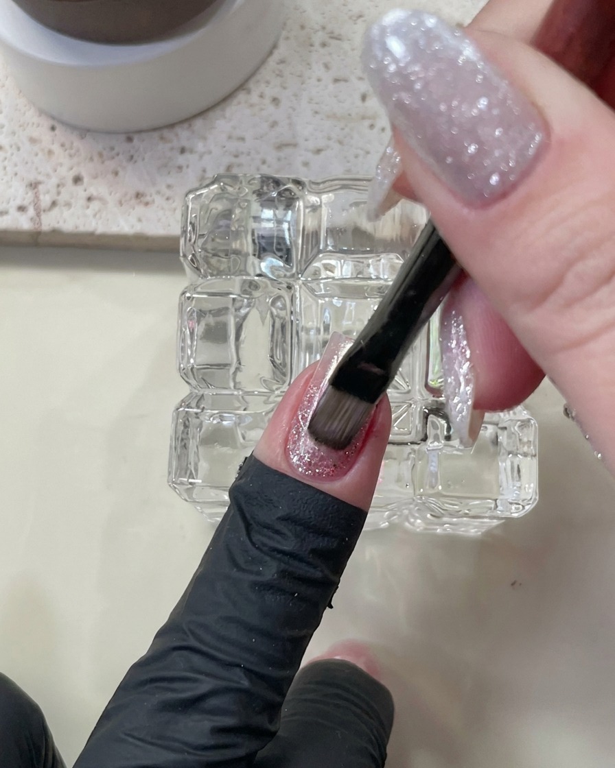Un pinceau appliquant un vernis gel œil de chat nude sur les couches dongle existantes.