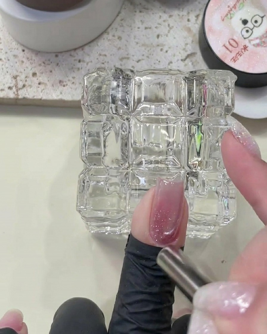 Vue rapprochée dun ongle maintenu avec un aimant pour façonner le pigment magnétique sur la base de diamants pailletés.