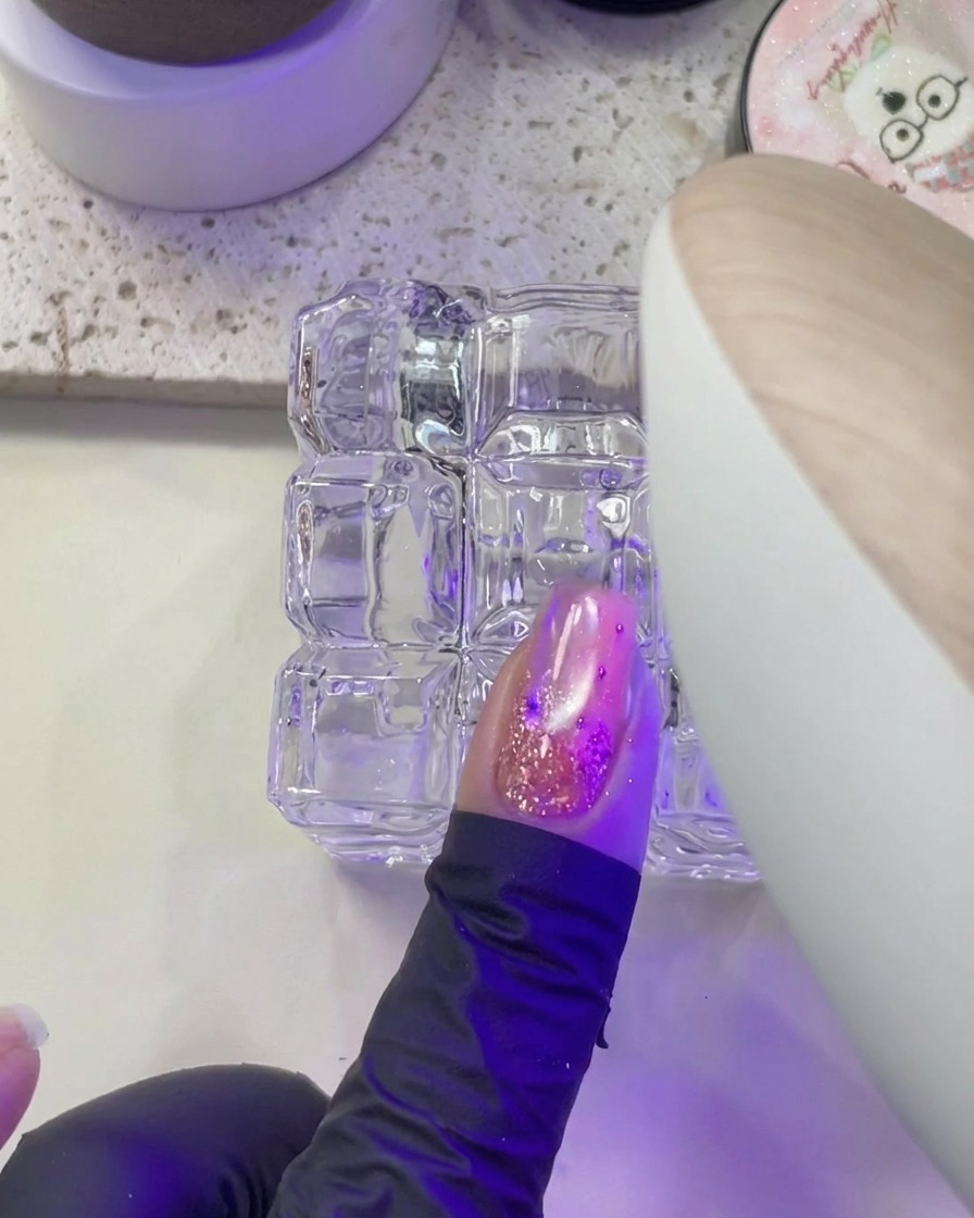 Une main plaçant un ongle sous la lumière violette dune lampe UV/LED pour la catalysation.