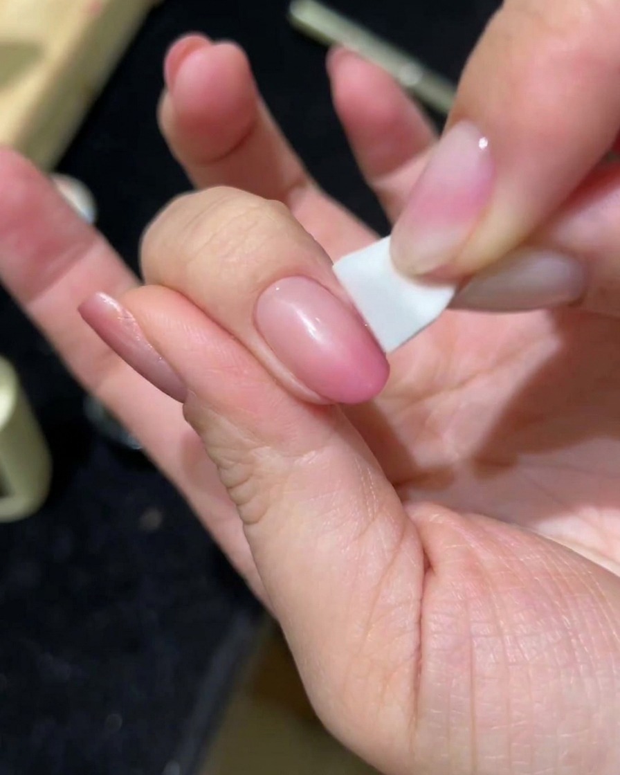 Une main tapotant une deuxième couche de gel cat-eye rose sur un ongle à laide dune éponge.