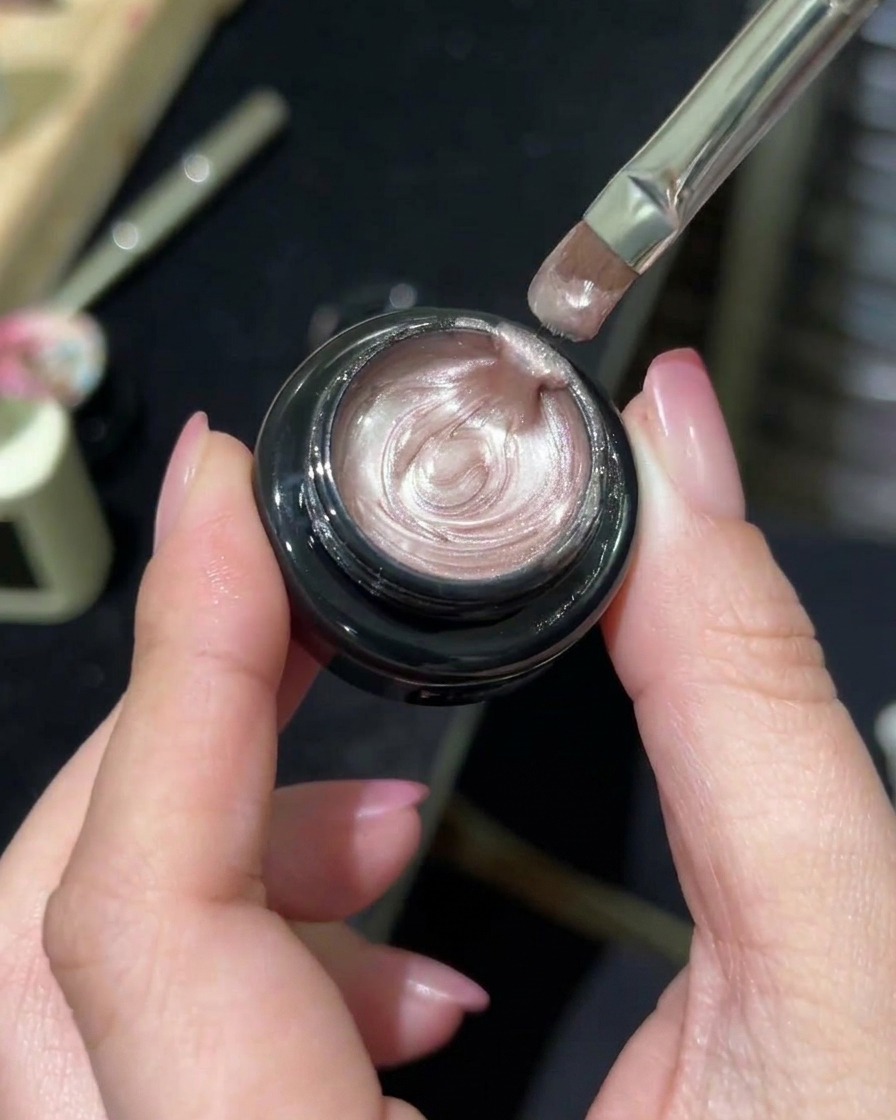Un pinceau à ongles professionnel prélevant un gel magnétique à effet aurora scintillant dans un pot.