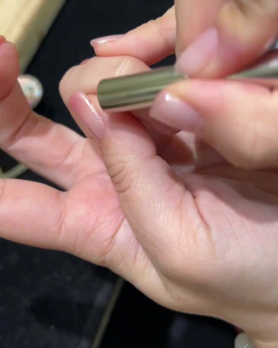 Une baguette magnétique tenue au-dessus dun ongle enduit de gel cat-eye, montrant le pigment bouger pour créer leffet magnétique.