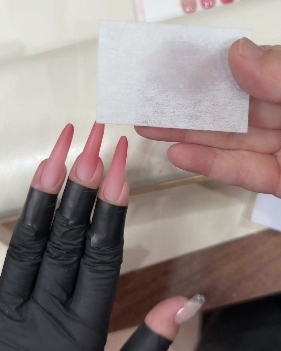 Un pinceau à gel appliquant un top coat transparent et brillant sur un ongle ombré rose fini.