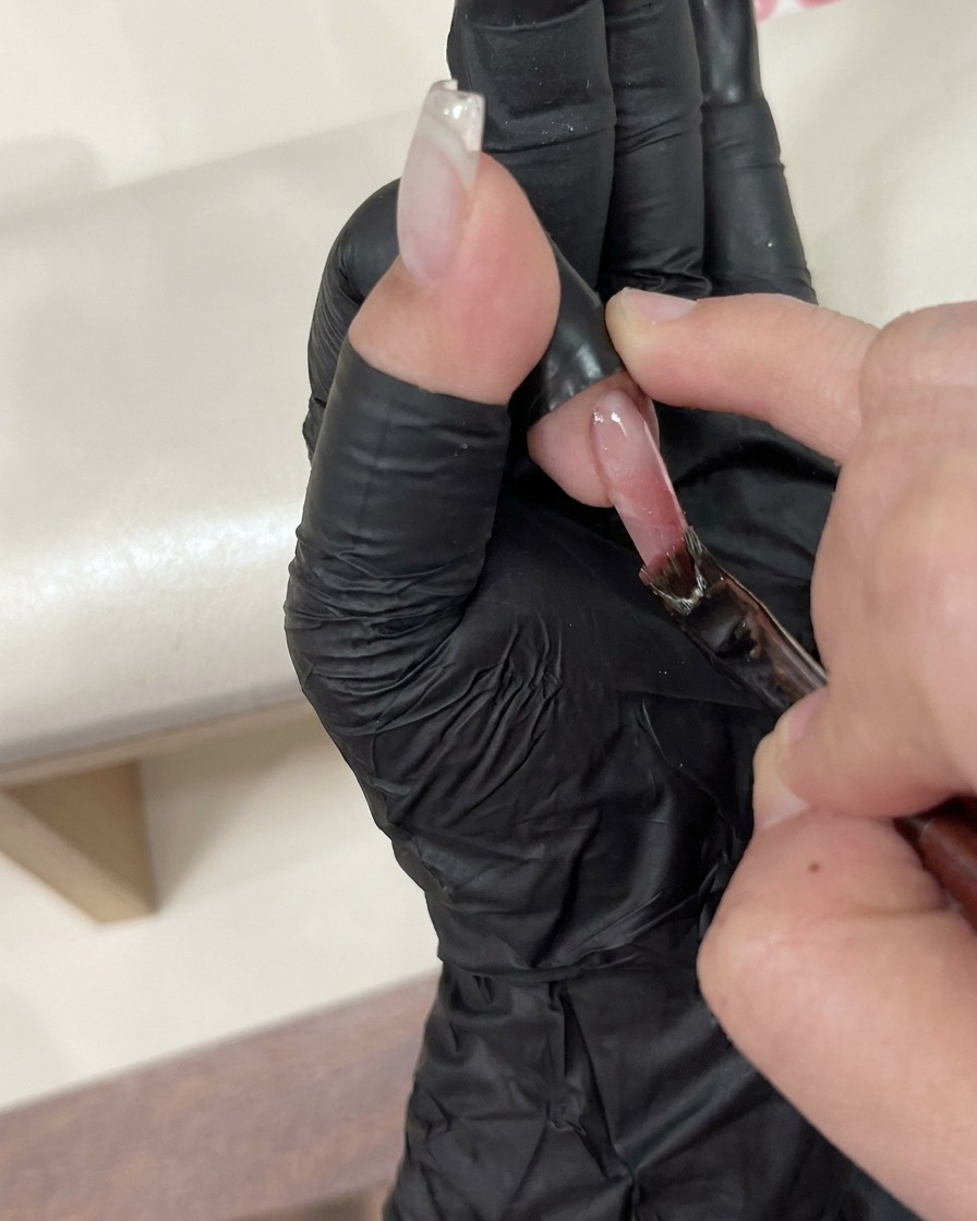 Une pince à épiler plaçant soigneusement un petit bijou décoratif sur un ongle humide recouvert de top coat.