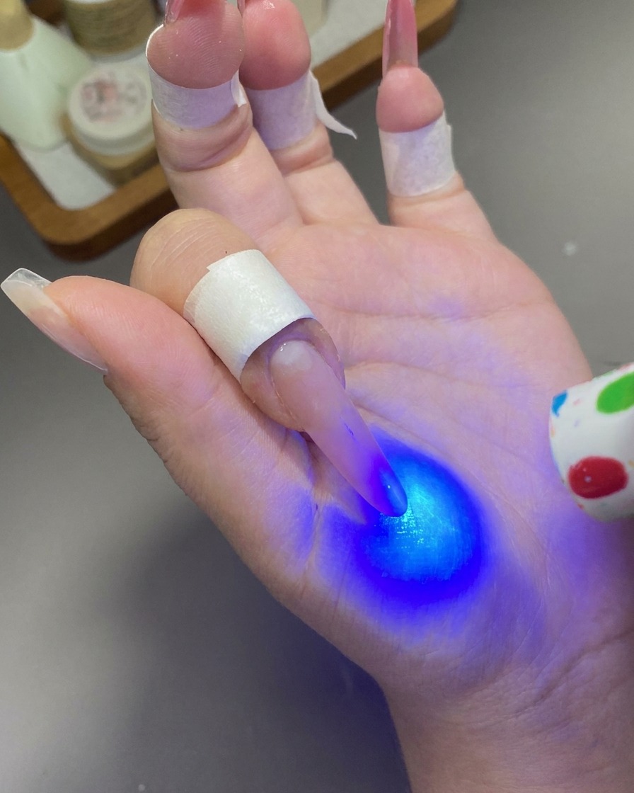 Une mini lampe UV/LED portable émettant une lumière bleue sur un ongle.