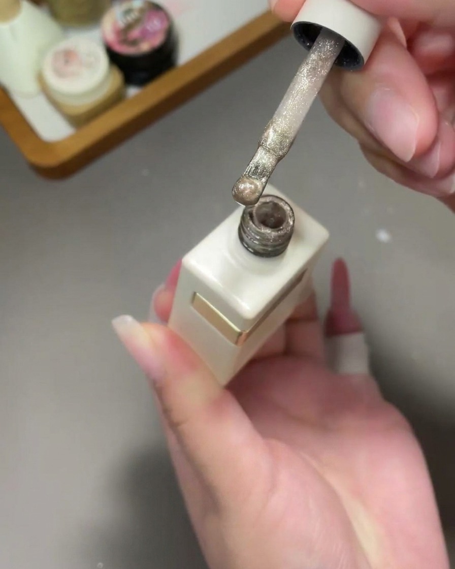 Un pinceau applique un vernis cat eye doré scintillant sur un ongle au dégradé rose.