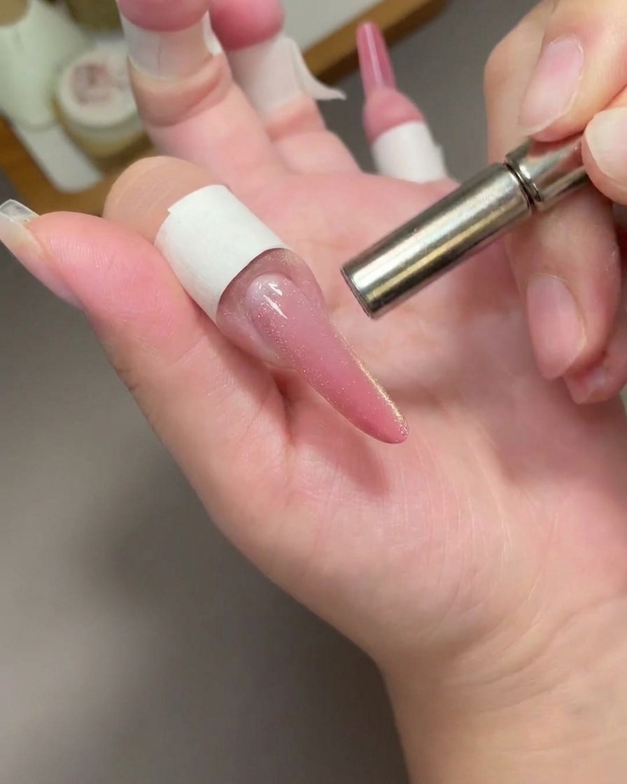 Gros plan sur un aimant métallique cylindrique survolant un ongle long rose cat eye pour déplacer les pigments.