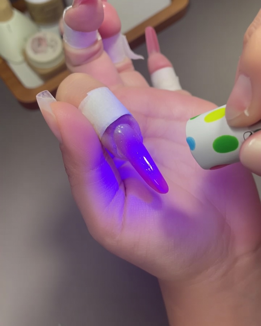 Une petite lampe UV à motifs pois utilisée sur un ongle au design cat eye violet-rose.