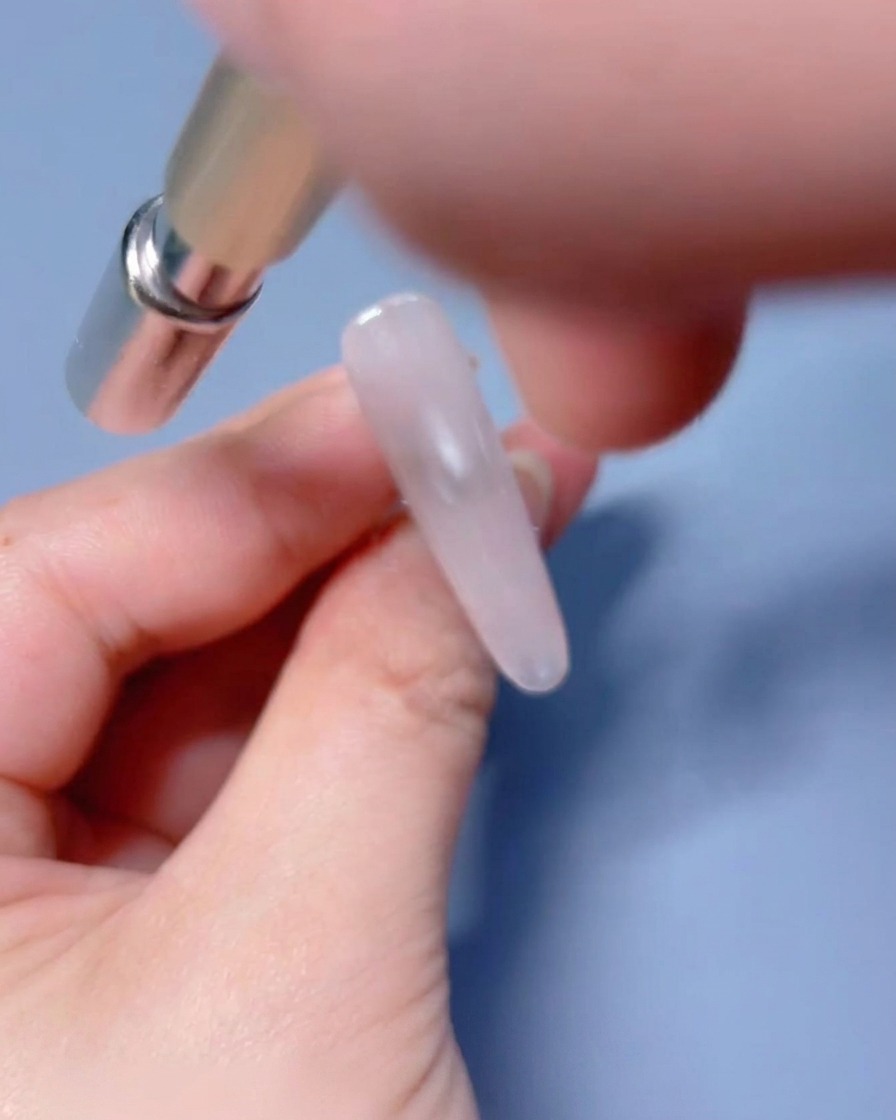 Un outil magnétique placé près de longle recouvert de gel humide pour manipuler les particules brillantes.