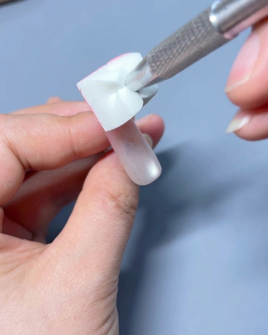 Un pinceau gel plat estompant délicatement la couleur rose pour créer un dégradé sur longle.