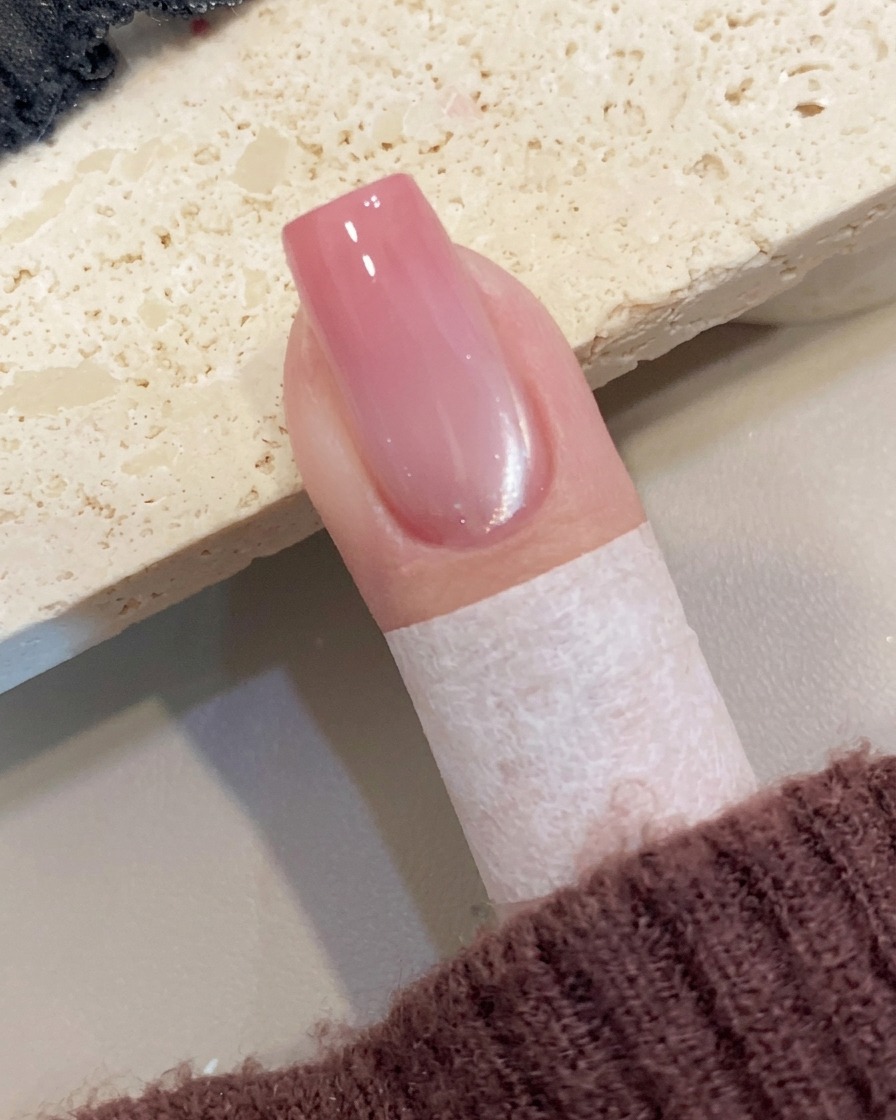 Vue rapprochée dune main retirant délicatement un ruban de protection sur la peau entourant un ongle manucuré.