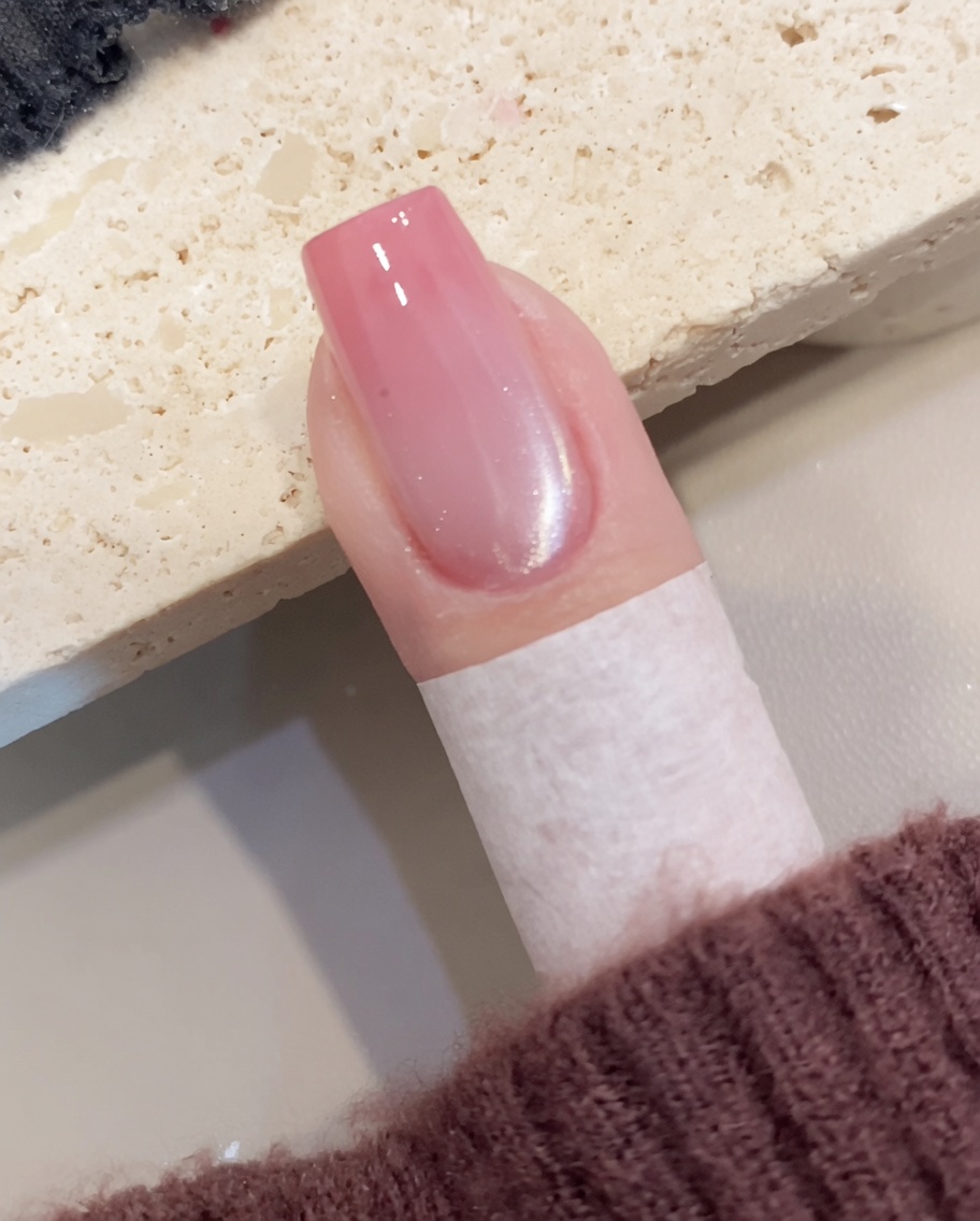 Vue rapprochée montrant un pinceau appliquant un vernis gel œil de chat scintillant et translucide sur un ongle préparé.