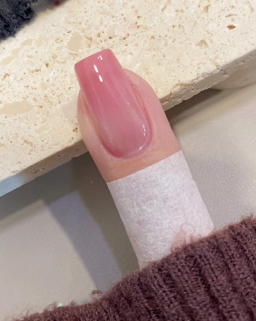 Un pinceau appliquant une couche finale de top coat transparent ultra-brillant sur un ongle ombré pêche.