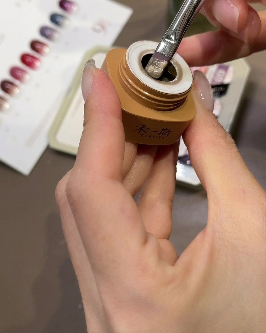 Un pinceau appliquant du gel œil-de-chat beige pêche sur une capsule transparente.