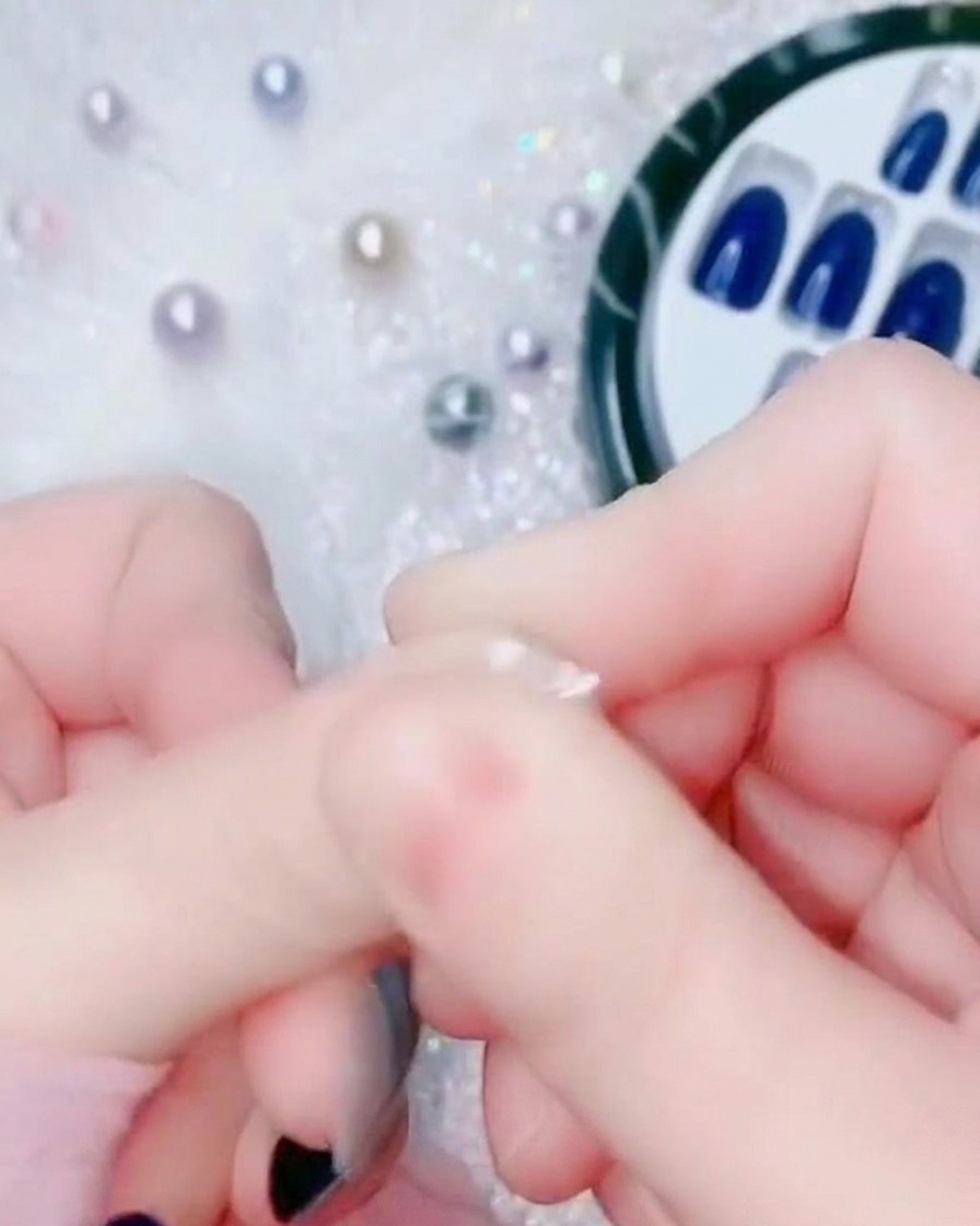 Gros plan dun doigt pressant la base dun faux ongle bleu électrique contre la zone de la cuticule naturelle.