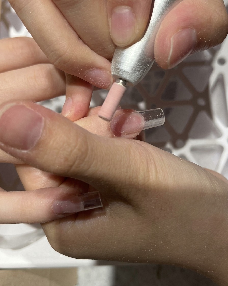 Une ponceuse estompant la jonction entre la capsule et longle naturel.