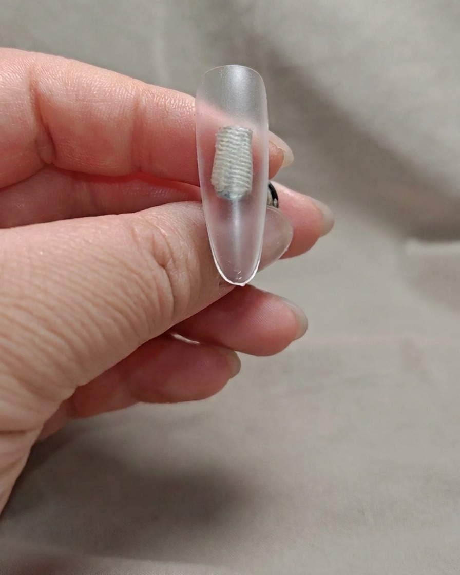 Un pinceau appliquant une fine couche de gel rose nude transparent sur la pointe dun ongle.