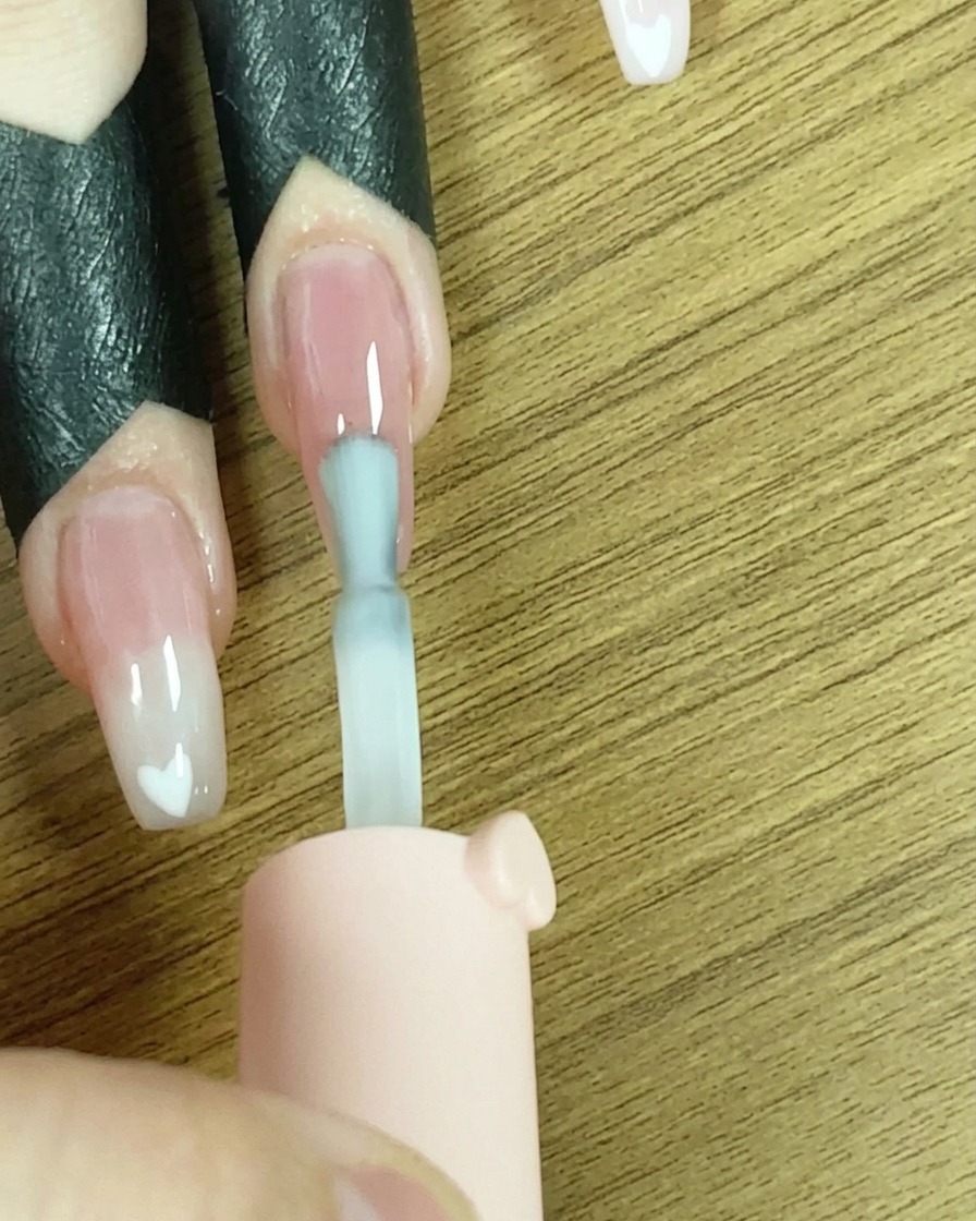 Un pinceau appliquant une ligne de vernis gel blanc sur le bout de longle.