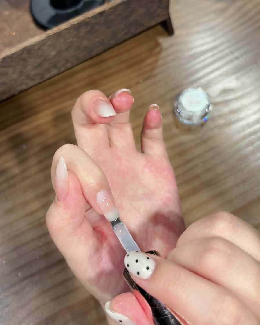 Un pinceau appliquant un top coat transparent sur un ongle dégradé effet chrome fini.