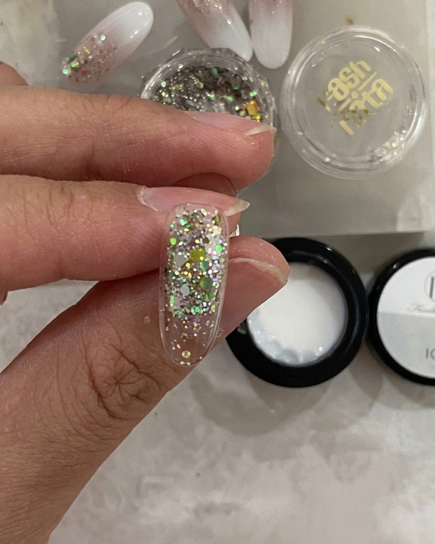 Vue rapprochée dune capsule à ongle dans une lampe UV, avec la couche de paillettes en cours de durcissement.