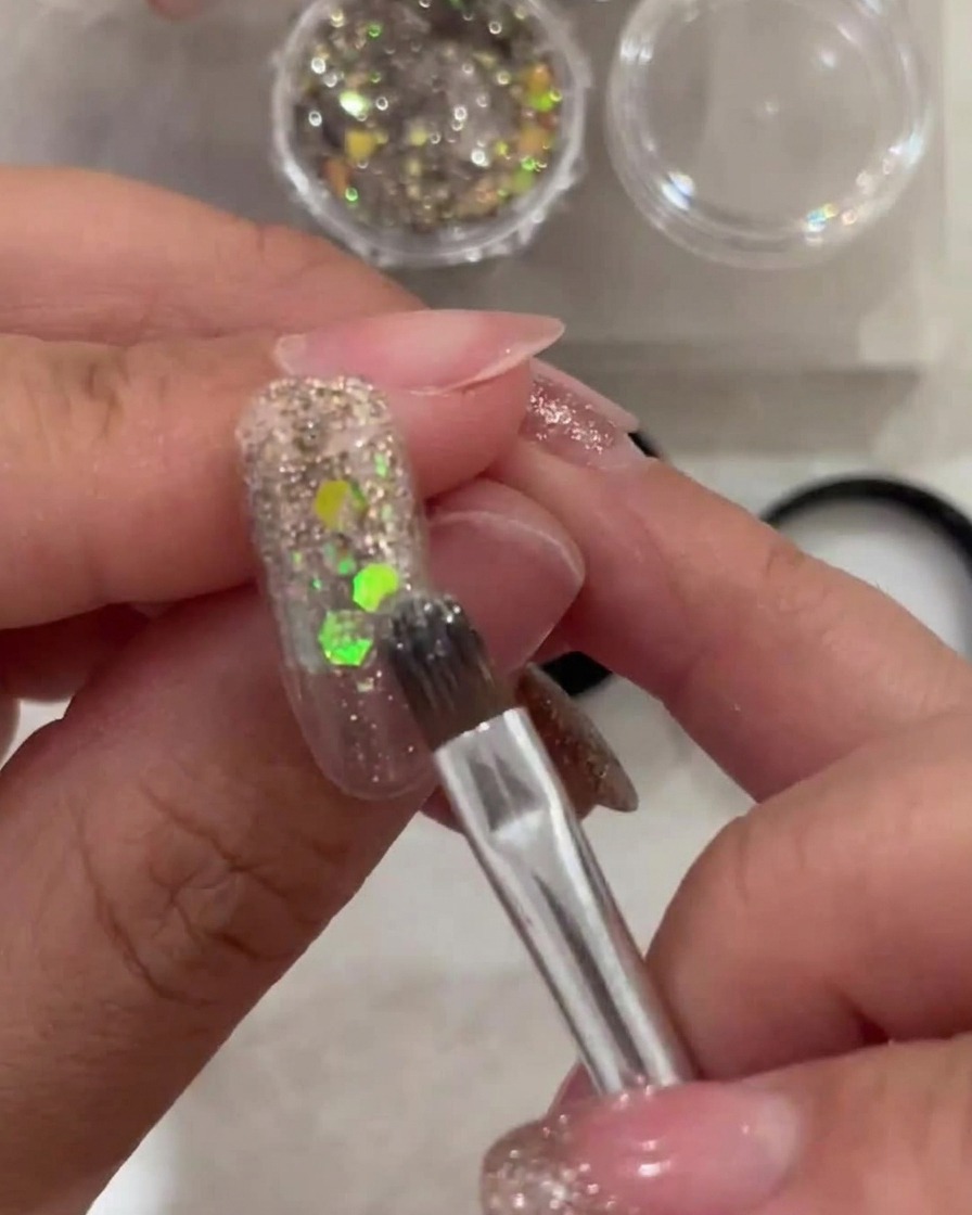 Un pinceau applique une fine couche de gel blanc transparent sur le bout dun ongle, en estompant vers la zone des cuticules.