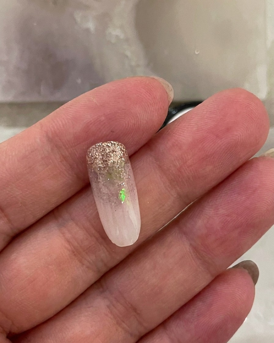 Un ongle avec le dégradé blanc laiteux, reposant dans une lampe UV allumée.